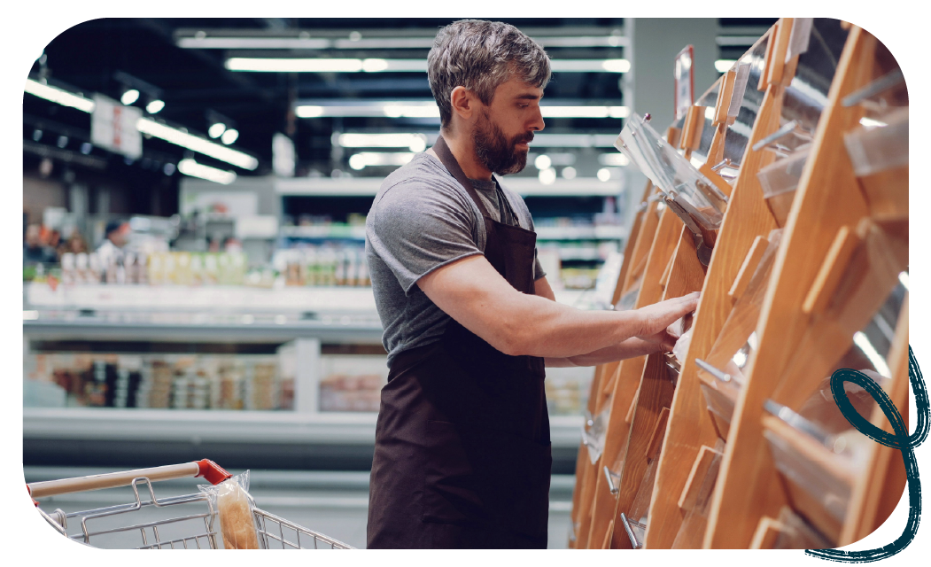 A grocery store employee in an apron arranging bread on wooden display shelves.