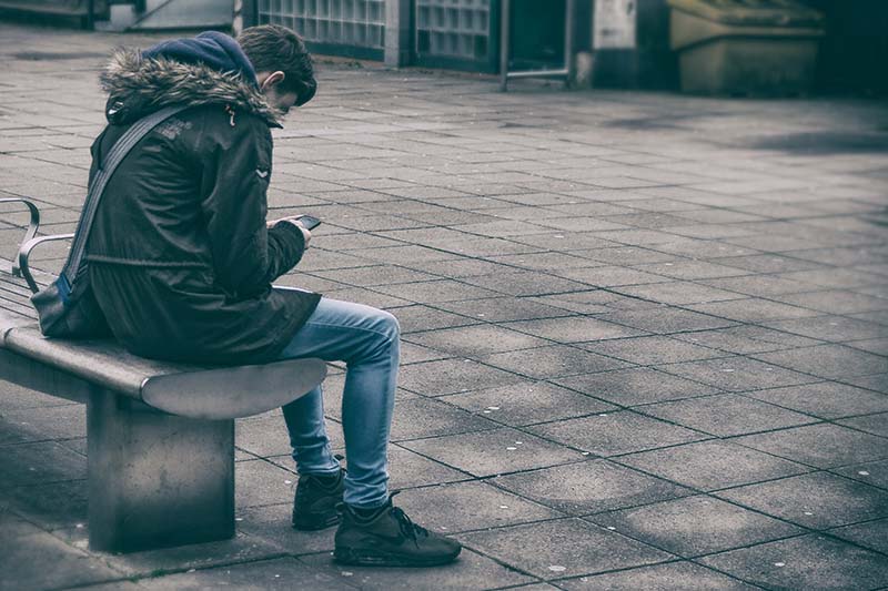 man texting while sitting on bench